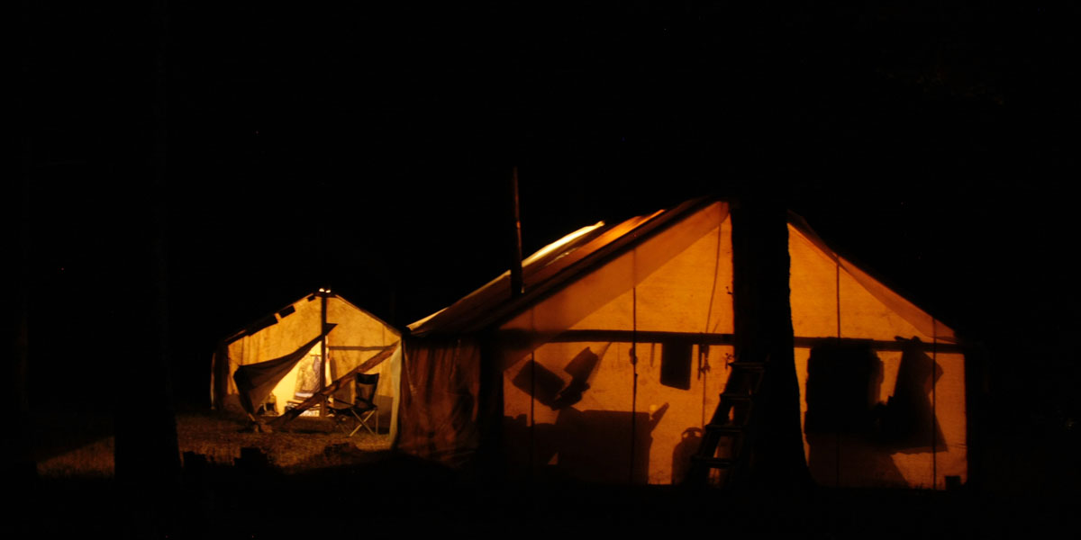 canvas wall tents at night with silhouettes